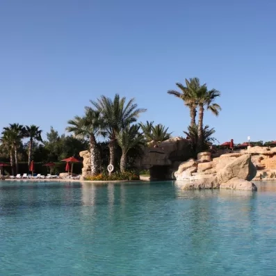 Grande piscine paysagère avec rochers artificiels et palmiers dans les jardins de l'hôtel Sahara Beach Monastir.