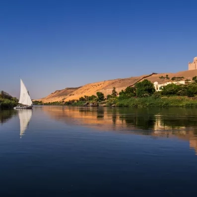 Felouque naviguant sur le Nil au coucher du soleil, paysage serein, croisière Secrets des Pharaons, Égypte.