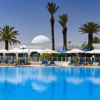 Grande piscine extérieure bleue bordée de parasols et de palmiers au Mondi Club Shems à Monastir.