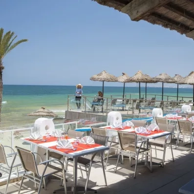 Terrasse ensoleillée du restaurant de plage avec parasols en paille face à la mer à Monastir.