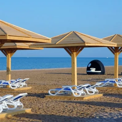 Plage privée avec parasols en bois et transats pour vacances détente à Hurghada, Égypte.