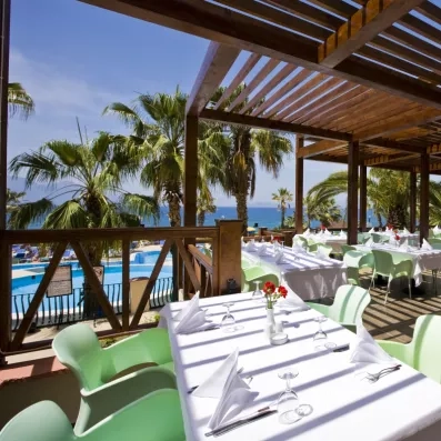 Une pergola en bois abrite des tables, offrant un cadre ombragé et rafraîchissant face aux palmiers.