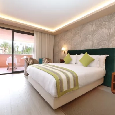 Chambre avec un grand lit de deux places, une tête de lit en vert foncé et une porte fenêtre donnant sur la terrasse 