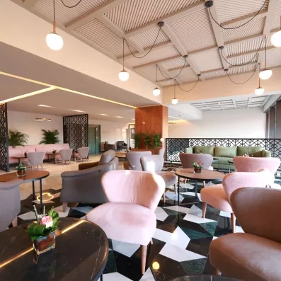 bar et hall d'entrée décoré avec des chaises en rose, vert et gris et des tables basses et des plantes au milieu