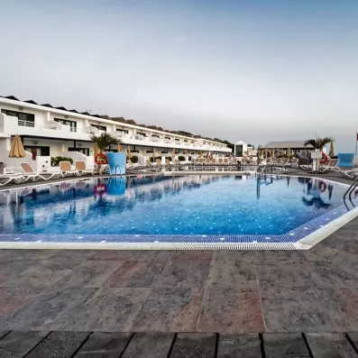 Une vaste piscine extérieure bordée de transats, située au pied d'un complexe de bâtiments.
