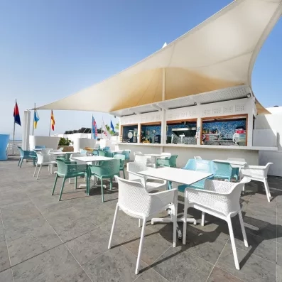 Une terrasse ensoleillée dotée d'un bar blanc moderne, avec des tables et chaises.
