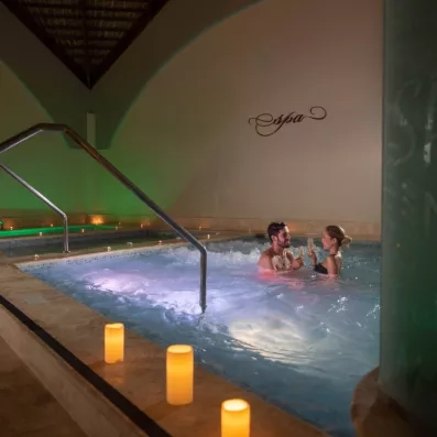 Un spa intérieur avec un bassin d'hydrothérapie éclairé par des bougies.