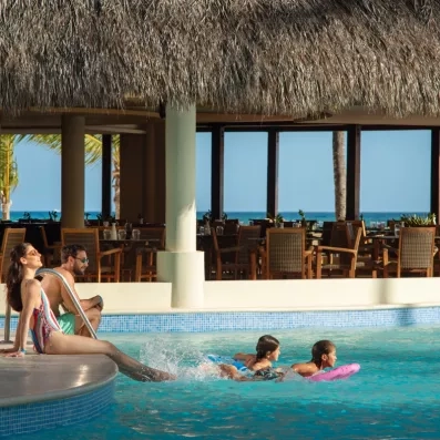 Une famille au bord de la piscine couverte par un toit en chaume traditionnel, offrant une vue sur l'océan.