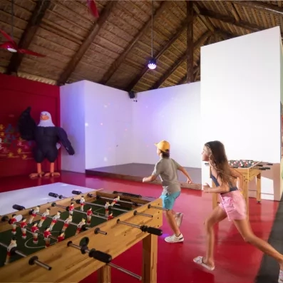 Une salle de jeux intérieure animée où des enfants s'amusent autour d'un baby-foot.