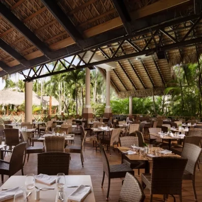 Une terrasse de restaurant couverte, entourée d'une végétation et meublée de nombreuses tables en bois.