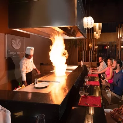Un chef réalisant une démonstration spectaculaire avec des flammes devant des clients.