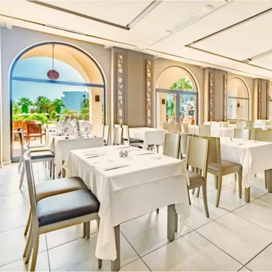 Salle de restaurant lumineuse de l'hôtel Palm Azur avec tables dressées et grandes arcades vue jardin.