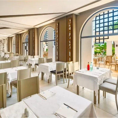 Espace de restauration élégant du Palm Azur avec nappes blanches et architecture méditerranéenne aux larges baies.