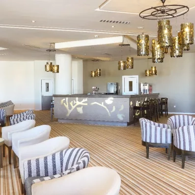 Bar intérieur design de l'hôtel Palm Azur avec luminaires dorés et fauteuils confortables à rayures.