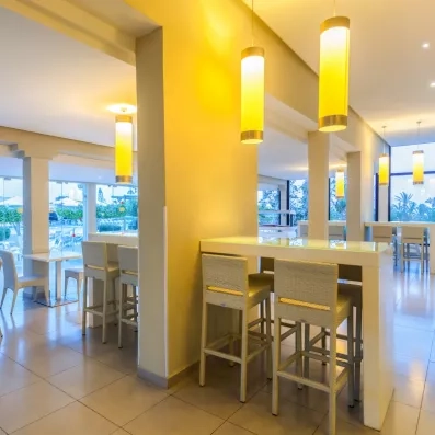 Bar moderne et lumineux du Djerba Aqua Resort avec chaises hautes en osier et luminaires design suspendus.