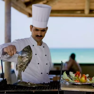 Chef cuisinier préparant du poisson grillé face à la mer au restaurant de plage du Djerba Aqua Resort.