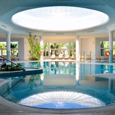 Piscine intérieure chauffée sous coupole lumineuse avec transats au spa du Royal Garden Palace à Djerba.