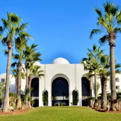 Façade blanche à coupoles et palmiers majestueux de l'hôtel de luxe Royal Garden Palace à Djerba.