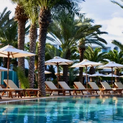 Transats alignés au bord d'une piscine bordée de palmiers tropicaux lors d'un séjour balnéaire à Djerba.