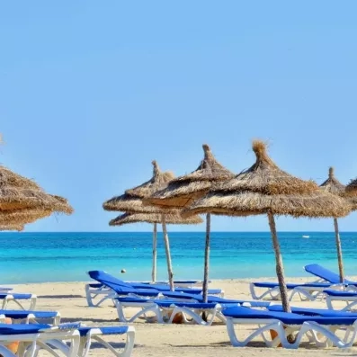 Plage de sable fin et parasols en paille devant la mer turquoise au Royal Garden Palace Djerba.