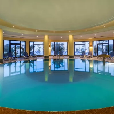 Grande piscine intérieure chauffée avec jets massants et larges baies vitrées pour se relaxer.