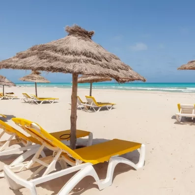 Plage de sable fin avec parasols en paille et transats jaunes au César Thalasso à Djerba.