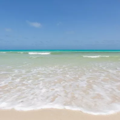 Eaux cristallines et vagues d'écume blanche sur la plage de sable blanc du César Thalasso.