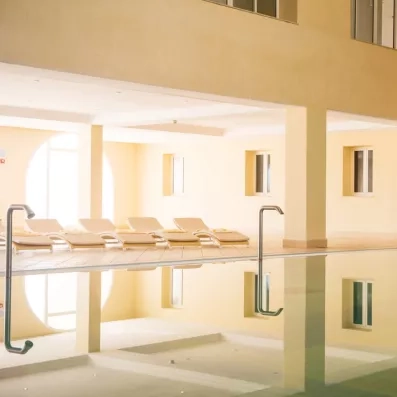 Chaises longues alignées au bord d'une piscine intérieure lumineuse pour un séjour bien-être à Djerba.