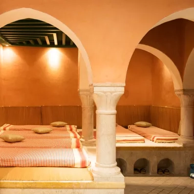 Salle de repos traditionnelle du spa avec lits de relaxation et colonnes en pierre sculptée.
