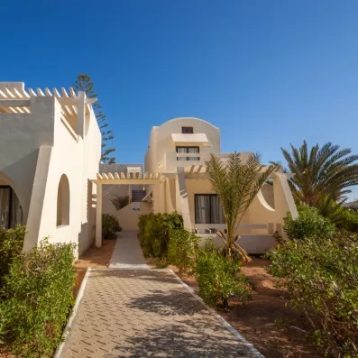 Allée pavée entre les bungalows blancs et palmiers de l'hôtel de luxe César Thalasso à Djerba.