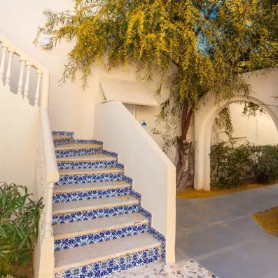 Escalier extérieur orné de mosaïques bleues traditionnelles sous une glycine jaune au César Thalasso Djerba.