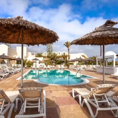 Piscine extérieure azur entourée de parasols en paille et transats pour un séjour détente à Djerba.