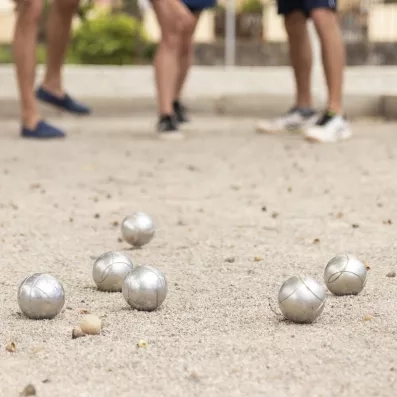 Plusieurs boules de pétanque en métal sont dispersées sur un terrain de sable.