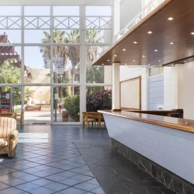 Le comptoir d'une réception d'hôtel moderne, éclairé par de larges baies vitrées donnant sur l'extérieur.