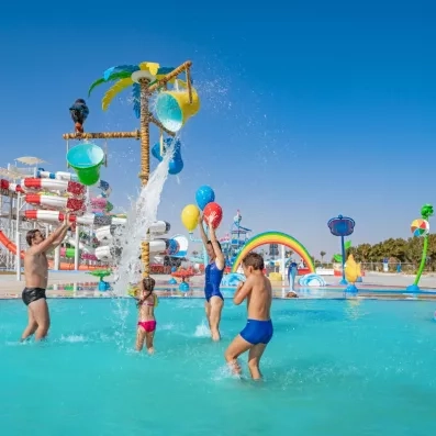 Famille s'amusant sous des seaux d'eau au parc aquatique du Mövenpick Resort Soma Bay.
