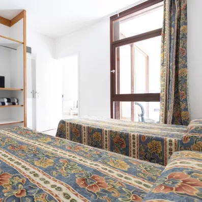 Une vue de l'intérieur d'une chambre montrant un lit douillet placé juste à côté d'une grande fenêtre en bois.