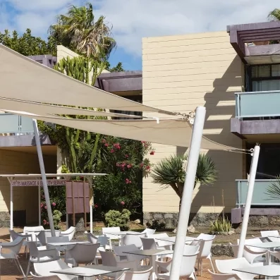 Une terrasse extérieure ensoleillée avec de nombreuses tables blanches abritées sous de grandes voiles.