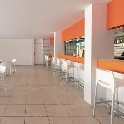 Une salle intérieure spacieuse avec des murs orange, équipée de chaises hautes blanches alignées le long d'un comptoir.