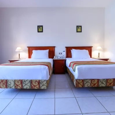 chambre avec deux lits une place séparé d'une table de nuit, deux petit tableaux décoratifs