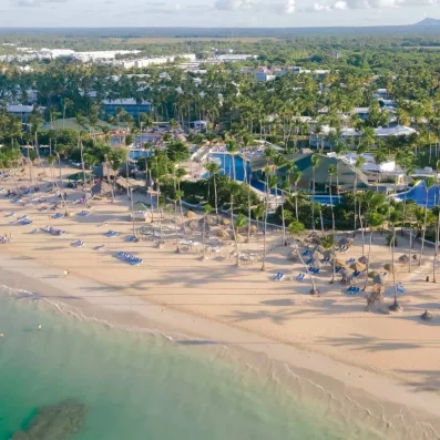 plage de sable, palmiers, végétation luxuriante, transats bleus et parasols paillote, pieds dans l'eau, piscines