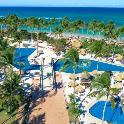 piscines avec accès direct sur la plage de sable, palmiers, végétation luxuriante, transats bleus et parasols paillote, pieds dans l'eau, océan et ciel bleus