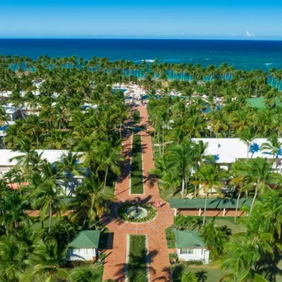 allée centrale partant de l'aquapark, passant par les boutiques et bars et menant à la plage et l'océan, végétation importante, nombreux palmiers, piscines, eau et ciel bleus