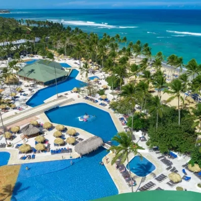 piscines avec accès direct sur la plage de sable, palmiers, végétation luxuriante, transats bleus et parasols paillote, pieds dans l'eau, océan et ciel bleus