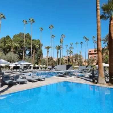 La piscine extérieur de l'hôtel et transats au bords avec des parasols et des palmiers