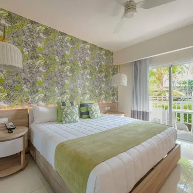 chambre double standard lit double avec chevet, baie vitrée donnant sur un balcon avec table et chaises, vue sur le jardin et les palmiers