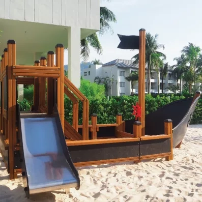 Une aire de jeux extérieure avec une structure en bois en forme de bateau pirate posée sur du sable.