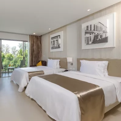 Une chambre d'hôtel avec deux lits doubles, s'ouvrant sur un balcon avec vue sur la verdure.