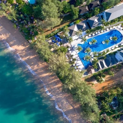 Vue aérienne de l'hôtel bordé par une plage aux eaux turquoise, avec une grande piscine nichée au cœur d'une végétation tropicale.