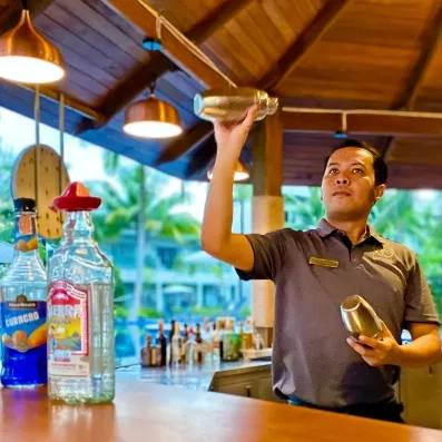 Un barman prépare un cocktail derrière un bar en bois exotique.
