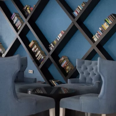 Un coin salon confortable avec des fauteuils bleus, devant une bibliothèque.